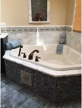 Corner tub with a marble deck and mosaic tile apron
