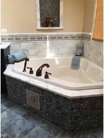 Corner tub with a marble deck and mosaic tile apron