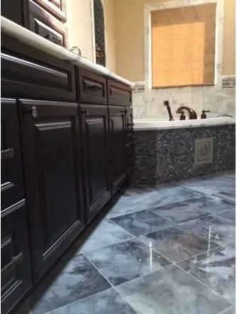 Dark vanity cabinets beside a tub faced in stone mosaic tile