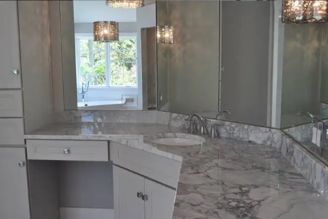 Grey marble vanity with a seated makeup station and glass shower beyond