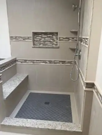 Grey tiled shower with a glass mosaic band and a stone bench