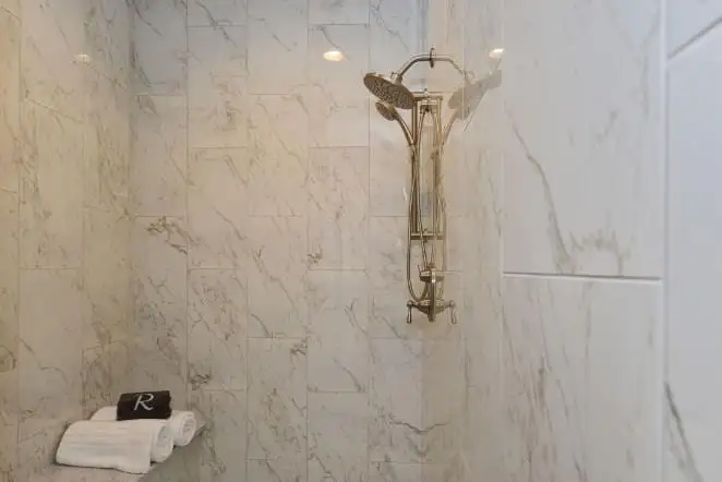 Marble shower wall with chrome fixtures and a corner shelf