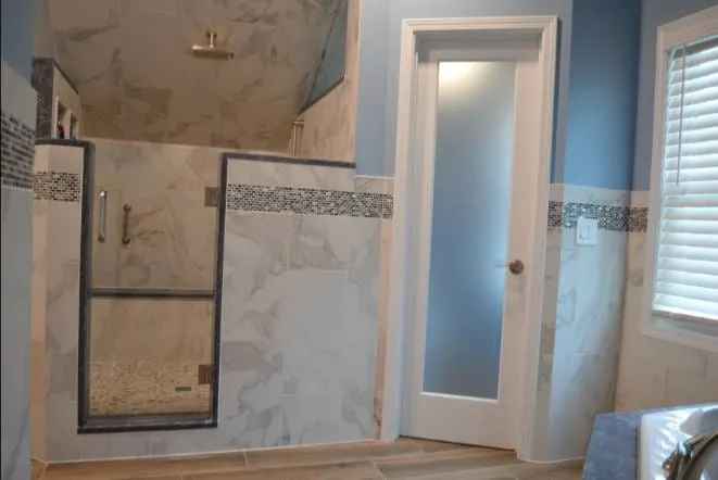 Marble tiled shower with a glass door and mosaic accent