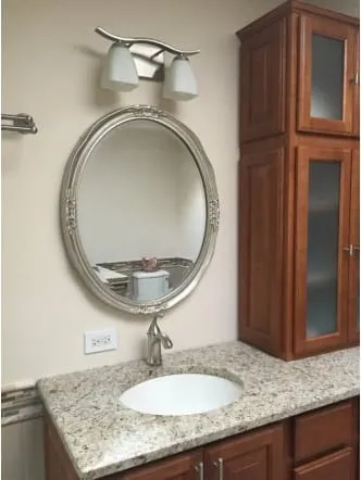 Oval mirror above a cherry bathroom cabinet with a stone top