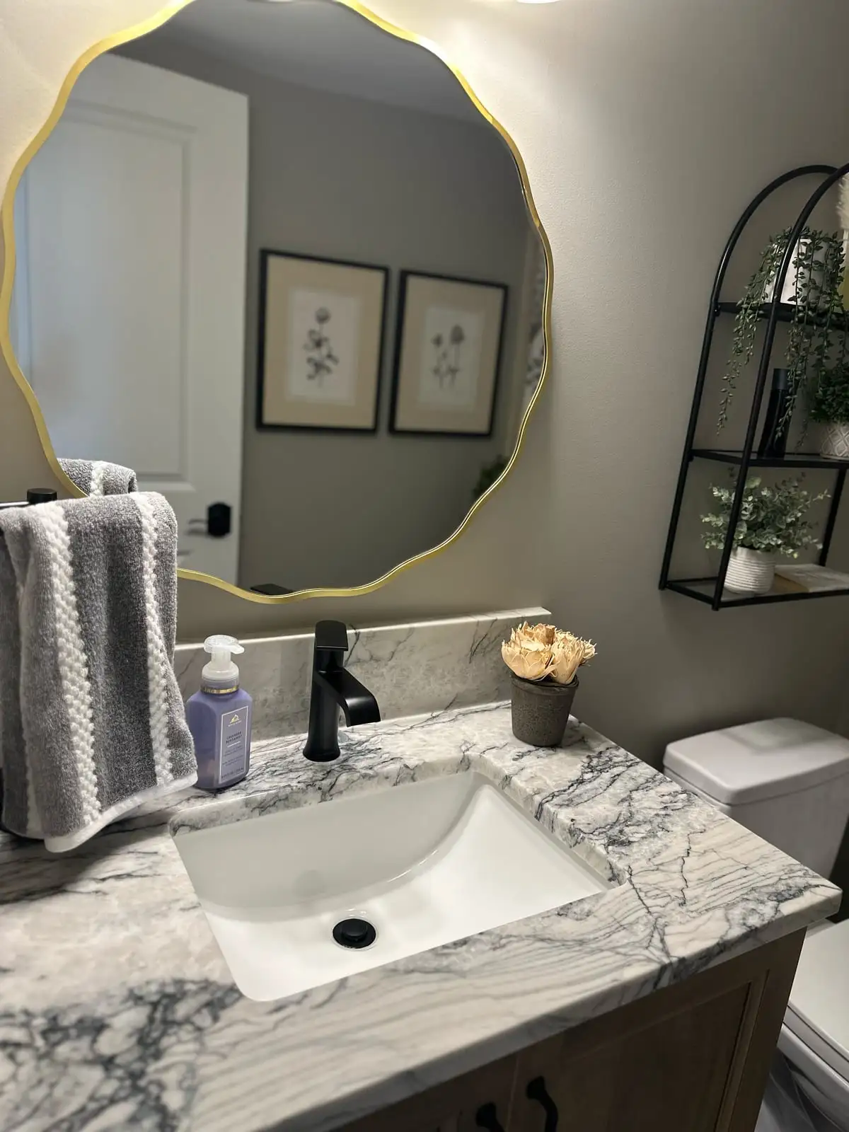 Powder-room vanity in grey-veined quartzite with a gold scalloped mirror and black faucet