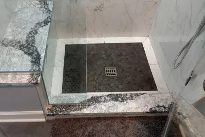 Shower floor in dark stone with a granite curb and marble walls