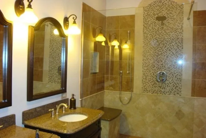 Travertine shower and vanity lit by wall sconces