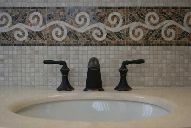 Travertine vanity top with an undermount sink and a scrolled mosaic tile border