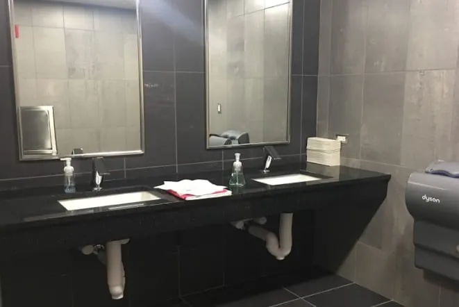 Commercial restroom with a long dark granite vanity and twin sinks