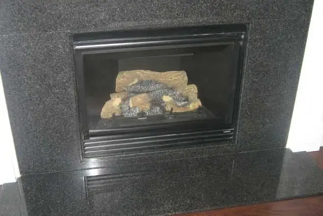 Black granite fireplace surround around a gas log insert