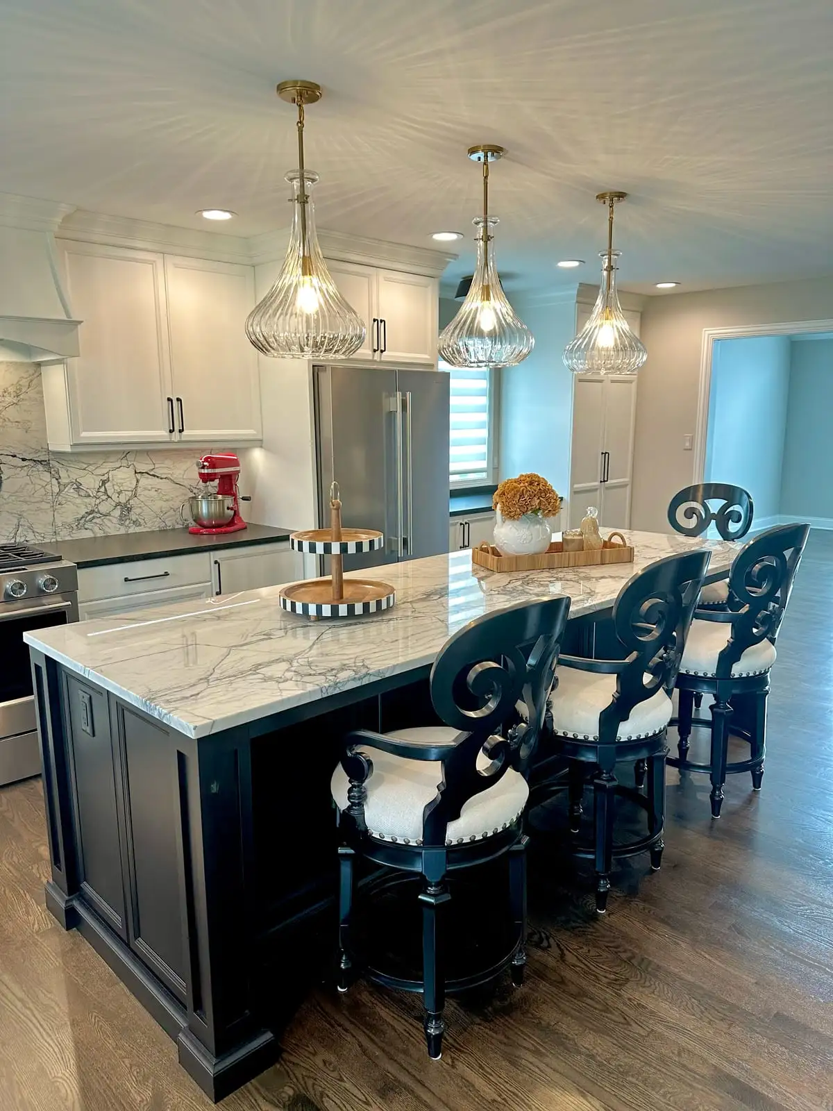 Black island with a white marbled stone top beneath crystal pendants in an open kitchen