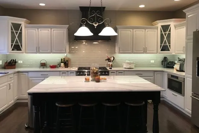 Black island with white quartz top in a white kitchen with glass-front cabinets