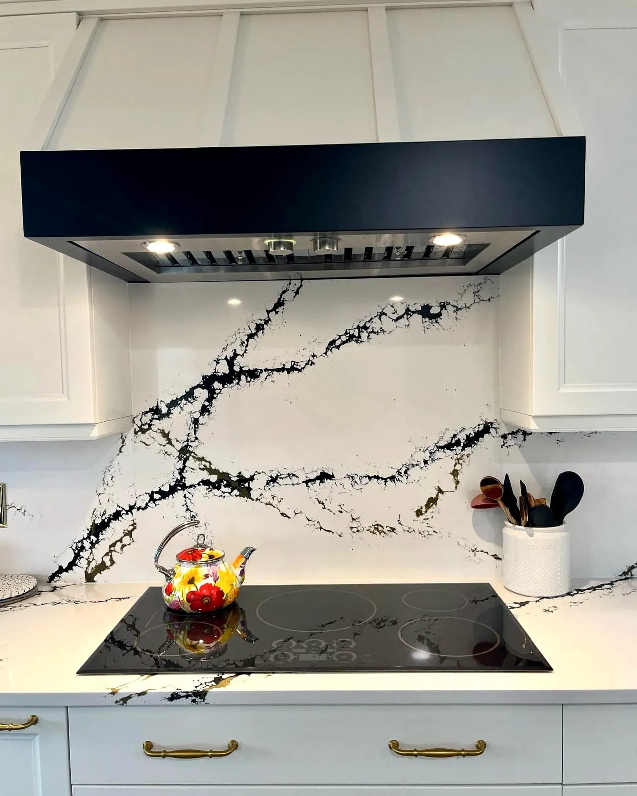 Boldly veined black-and-white quartz counters and full-height backsplash beneath a matte black range hood