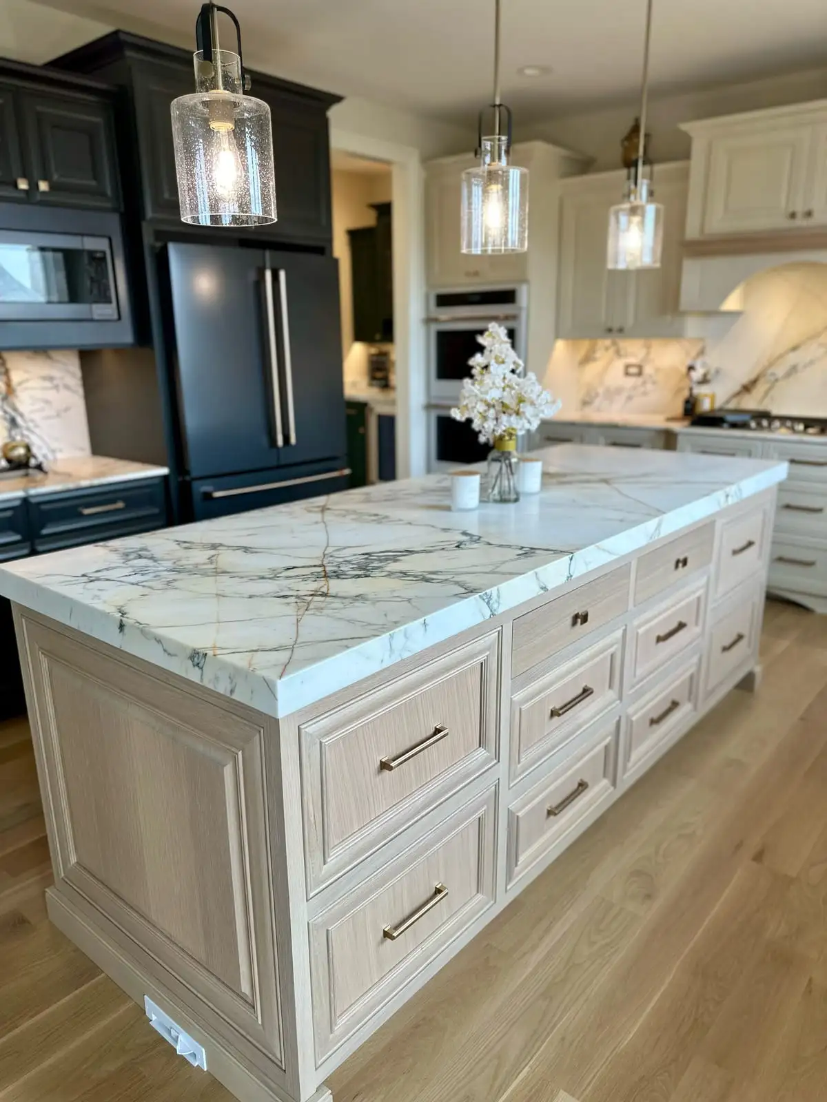 Calacatta-veined stone island over light-oak drawer cabinets beneath seeded-glass pendants