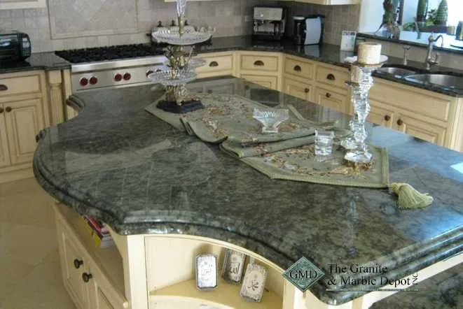 Curved green and grey granite island with a raised serving ledge and cream cabinetry