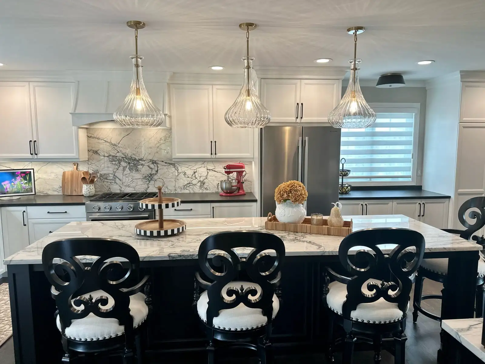Kitchen with a dramatically veined marble island and full-height backsplash beneath ribbed glass pendants