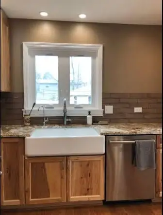 Farmhouse apron sink set into a gold granite countertop beneath a window