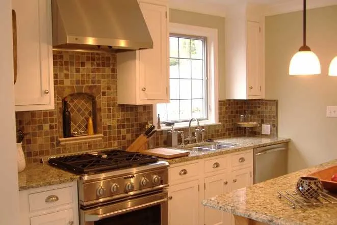 White cabinets with granite counters and a mosaic tile backsplash under a stainless hood