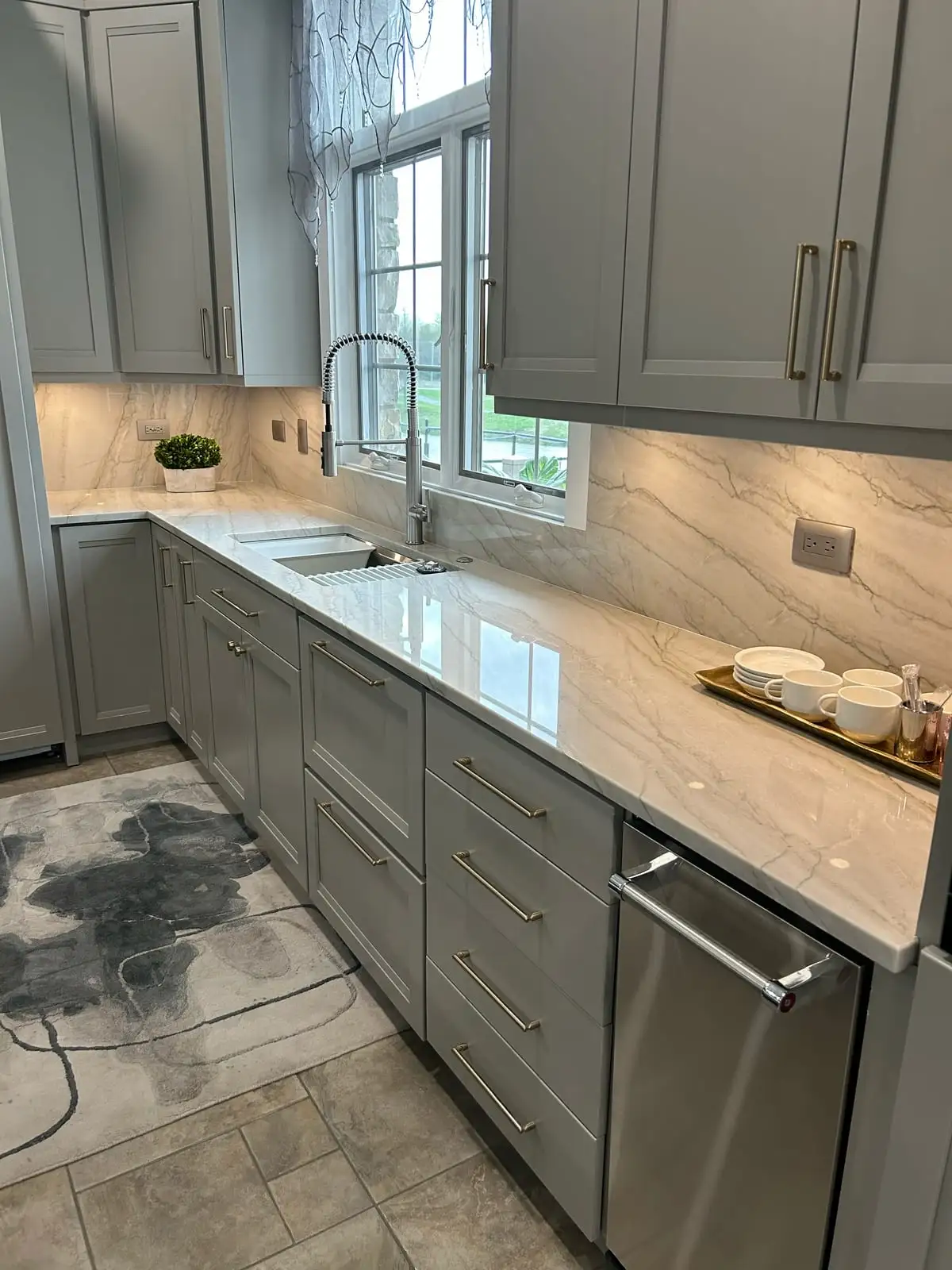 Grey shaker cabinets with softly veined quartzite counters and backsplash around a sink window