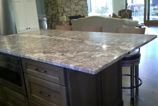 Large grey granite island with counter seating in front of a stone wall