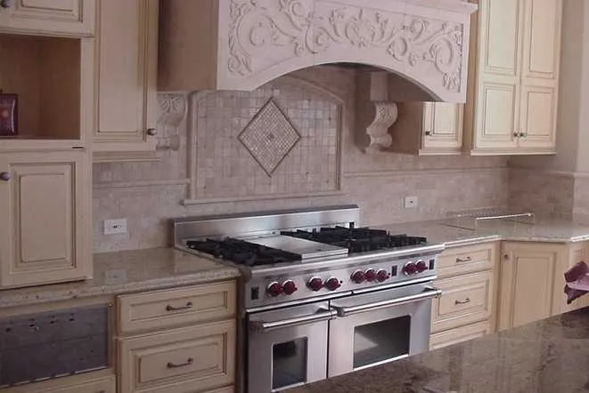 Light granite counters flanking a carved wood range hood above a professional gas range