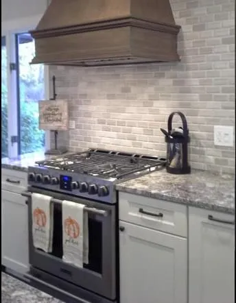 Marble-look countertops with a custom wood range hood and tile backsplash