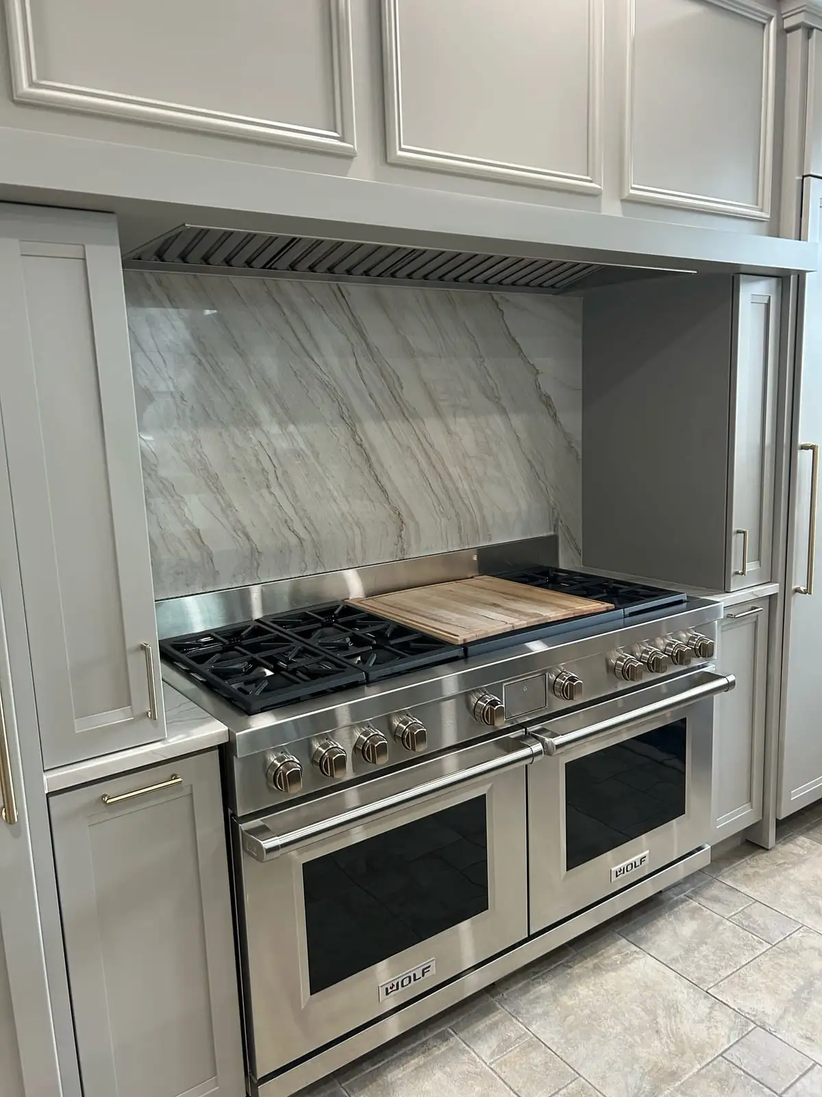 Quartzite slab backsplash behind a 48-inch professional range flanked by grey cabinets
