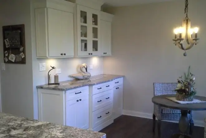 White cabinets with speckled granite counters below a chandelier
