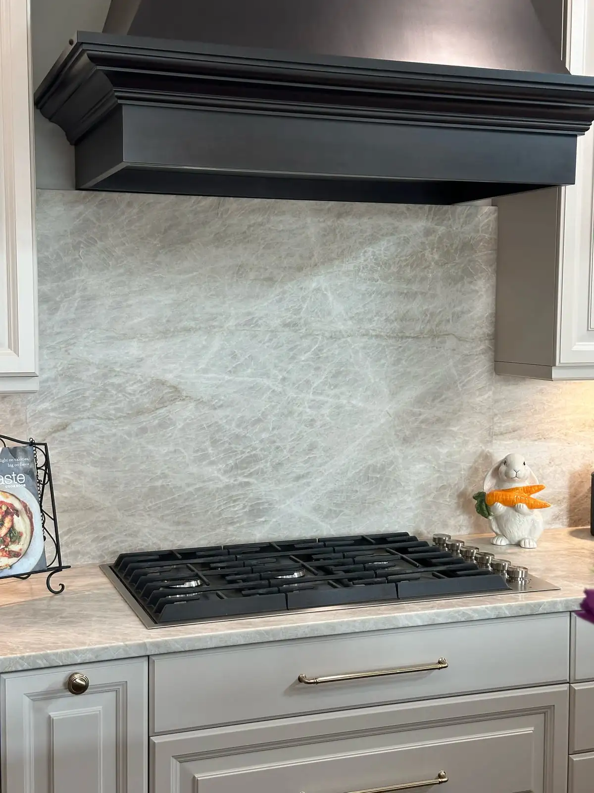 Full-height Taj Mahal quartzite backsplash beneath a black mantel-style range hood