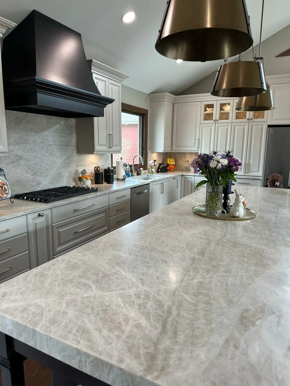 Vaulted grey kitchen with a long Taj Mahal quartzite island and brass pendants