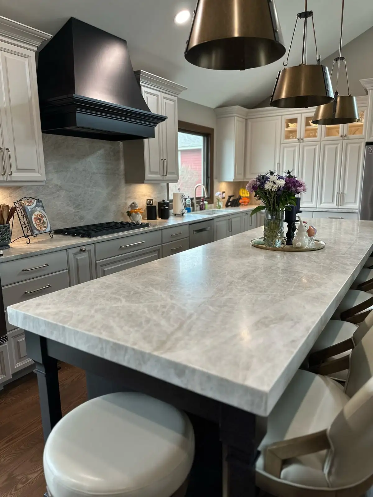 Taj Mahal quartzite island on a black base beneath brass cone pendants