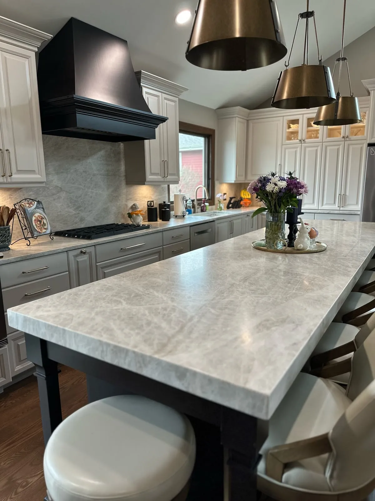Taj Mahal quartzite island on a black base beneath brass cone pendants