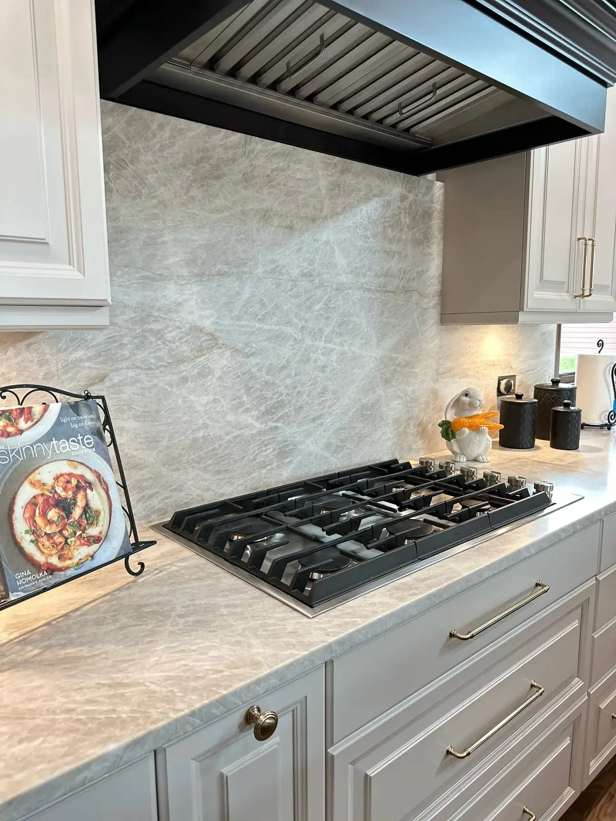 Taj Mahal quartzite counters and slab backsplash around a gas cooktop under a black hood