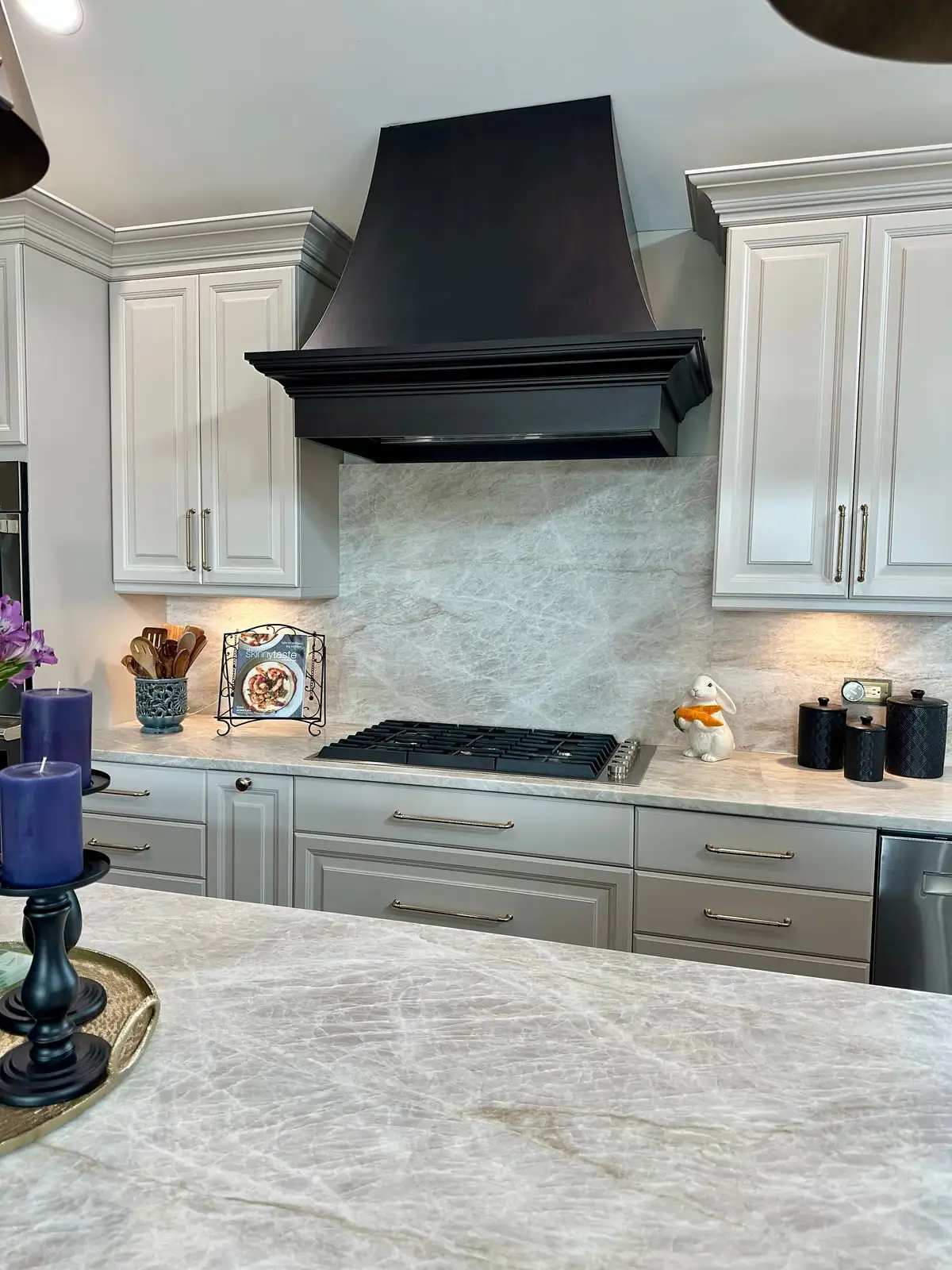 Taupe quartzite counters and full-height slab backsplash beneath a curved black range hood