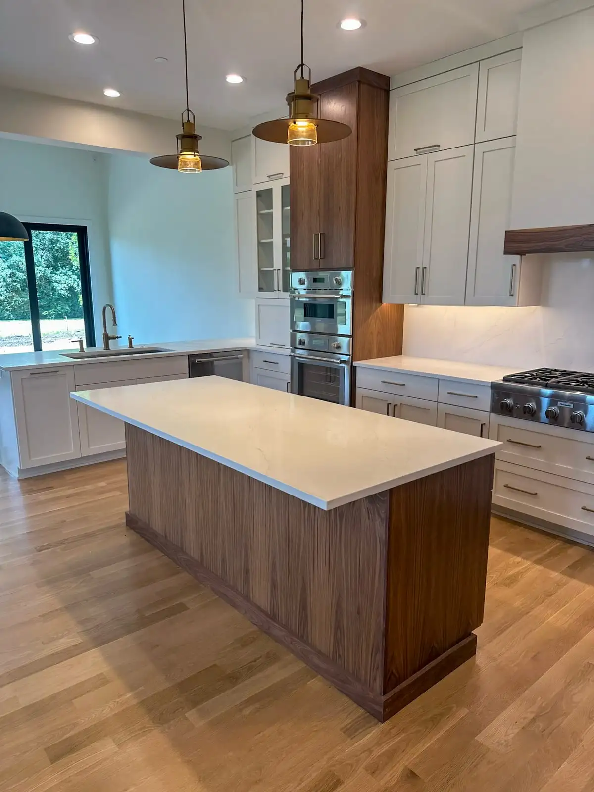 Modern kitchen with walnut tall cabinets and a white quartz island under brass pendants