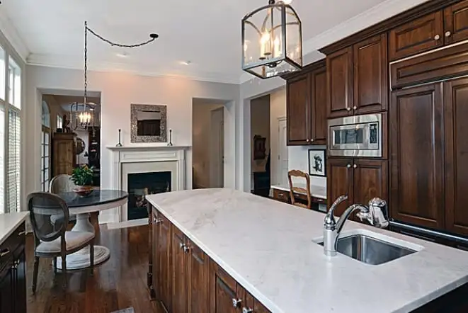 White stone island in a dark-cabinet kitchen open to a fireplace