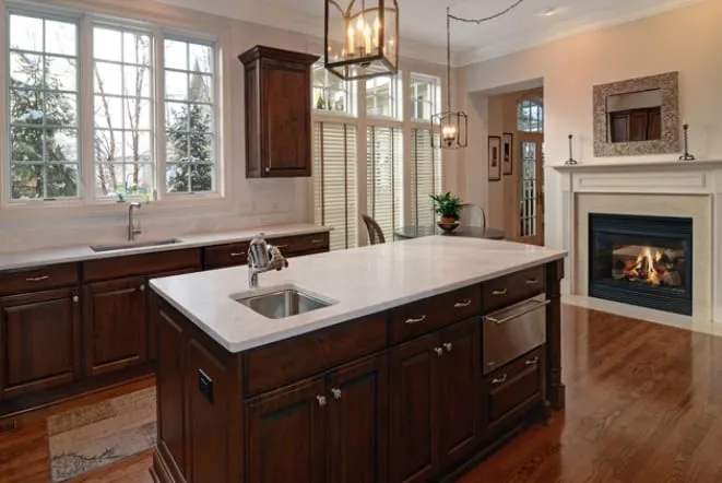 White stone island in a dark-cabinet kitchen opening onto a fireplace seating area