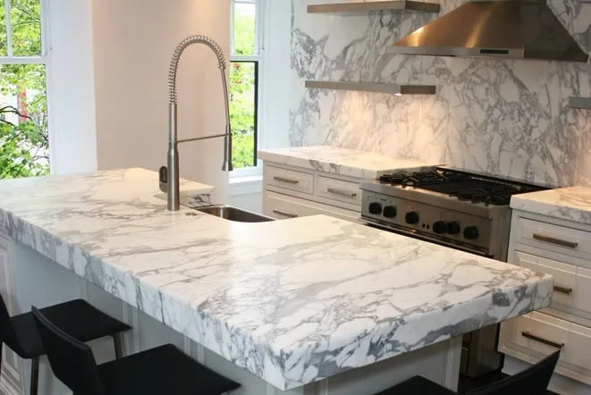 White marble-look island with a tall faucet beside a professional gas range