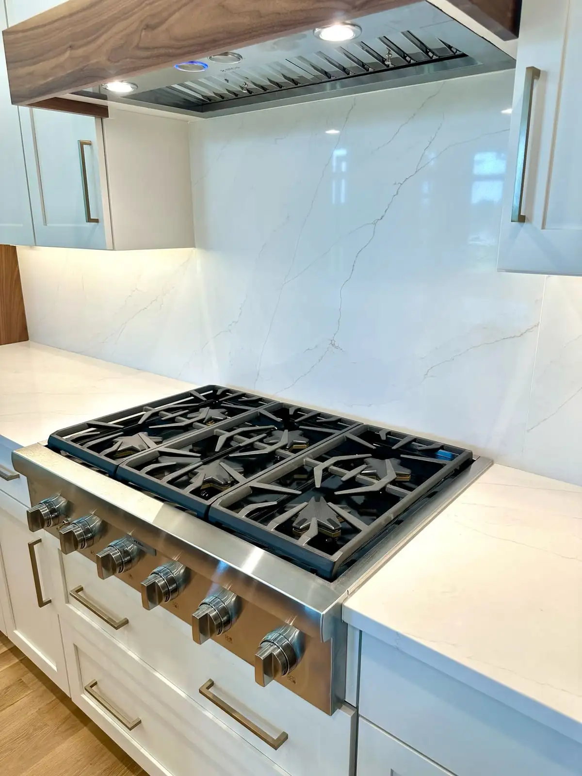Veined white quartz counters and backsplash around a professional gas rangetop beneath a walnut hood