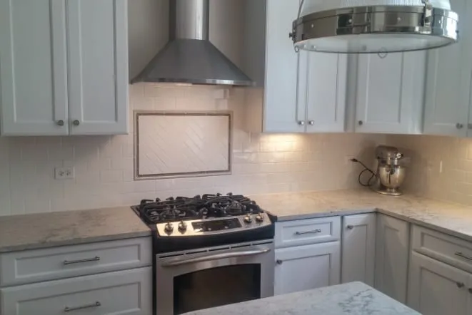 White quartz countertop beside a slide-in range under a stainless hood