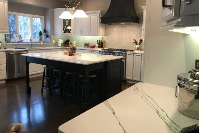 Dark island with white quartz top and pendant lights in a white kitchen