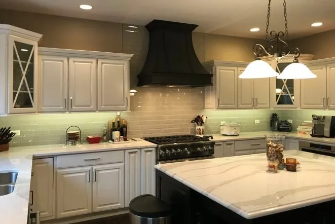 White quartz island in a white kitchen with a black custom range hood