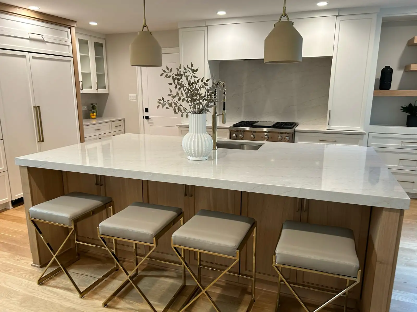 Bright white kitchen with an oversized quartz island, white-oak base and brass counter stools beside a professional range