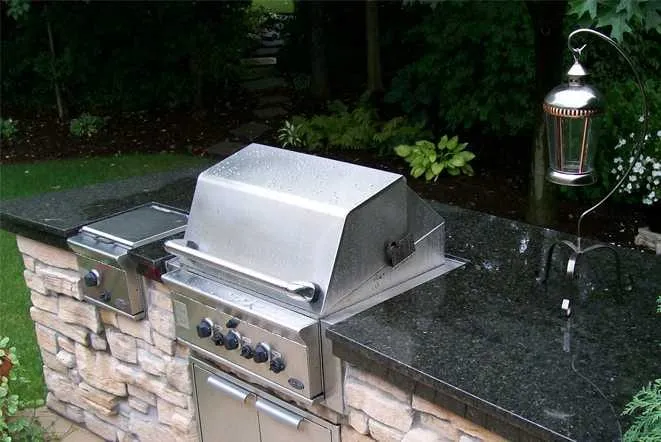 Stone grill island topped with black granite in a garden setting
