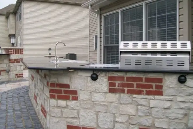 Outdoor kitchen with a bar sink and stone base built against the house